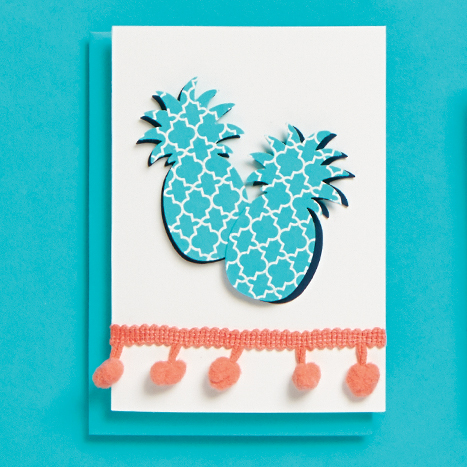 card with blue pineapples and pink pom pom trim on it