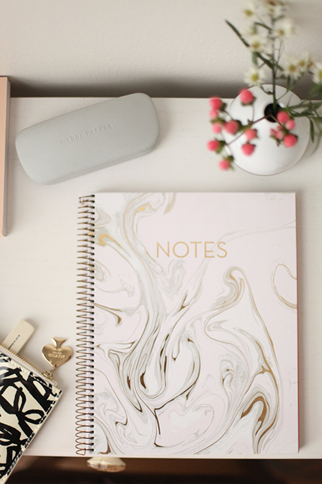 marble notebook on a desk with a vase of flowers and glasses